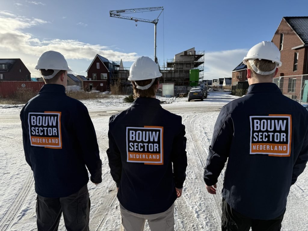 Drie vakmensen in werkjassen met logo kijken naar rijen woningen in aanbouw op een winterdag